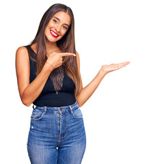 Wall Mural - Young hispanic woman wearing casual clothes amazed and smiling to the camera while presenting with hand and pointing with finger.