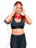 Fototapeta Koty - Young redhead woman wearing gym clothes and using headphones suffering from headache desperate and stressed because pain and migraine. hands on head.
