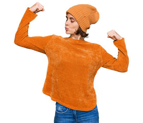 Poster - Young hispanic woman wearing casual clothes and wool cap showing arms muscles smiling proud. fitness concept.