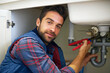 © YATrainer/peopleimages.com - Man, portrait and plumber with wrench for pipe repair, service or fix in home maintenance or indoor leak. Male person or handyman smile with water damage or sink of plumbing professional at the house