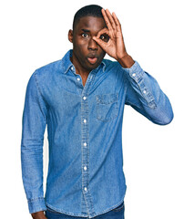 Wall Mural - Young african american man wearing casual clothes doing ok gesture shocked with surprised face, eye looking through fingers. unbelieving expression.