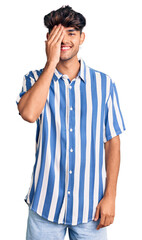 Canvas Print - Young hispanic man wearing casual clothes covering one eye with hand, confident smile on face and surprise emotion.