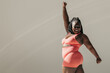 © gstockstudio - Full length of happy African plus size woman in sportswear doing stretching exercises in fitness studio