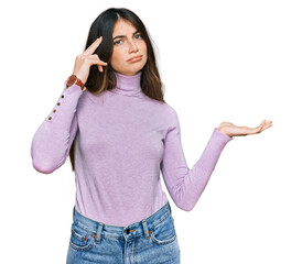 Wall Mural - Young beautiful teen girl wearing turtleneck sweater confused and annoyed with open palm showing copy space and pointing finger to forehead. think about it.