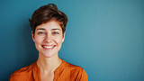 Fototapeta  - A woman with short brown hair and a bright orange shirt is smiling at the camera. She has a clean, fresh look and seems to be in a good mood