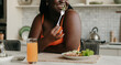 © gstockstudio - Close-up of plus size African woman enjoying healthy food for lunch at the kitchen