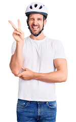 Canvas Print - Young handsome man wearing bike helmet smiling with happy face winking at the camera doing victory sign. number two.