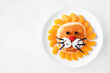 Cute child theme breakfast pancake in the shape of a lion face. Above view on a white marble background.