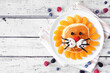 Fun child theme breakfast pancake in the shape of a lion face. Top view table scene on a white wood background.
