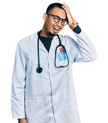 Wall Mural - Young african american man wearing doctor uniform and stethoscope surprised with hand on head for mistake, remember error. forgot, bad memory concept.