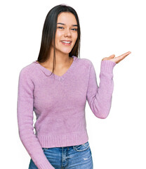 Wall Mural - Young hispanic girl wearing casual clothes smiling cheerful presenting and pointing with palm of hand looking at the camera.