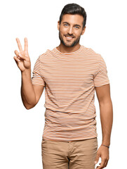 Wall Mural - Handsome hispanic man wearing casual clothes smiling looking to the camera showing fingers doing victory sign. number two.