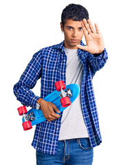 Poster - Young african amercian man holding skate with open hand doing stop sign with serious and confident expression, defense gesture