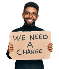 Wall Mural - Young african american man holding we need a change banner looking positive and happy standing and smiling with a confident smile showing teeth