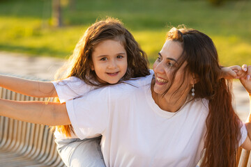 Happy mother having fun with her daughter outdoor - Family and love concept. Portrait of mother and daughter in the city park at summer sunset