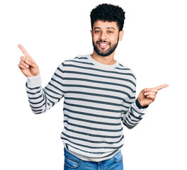 Wall Mural - Young arab man with beard wearing casual striped sweater smiling confident pointing with fingers to different directions. copy space for advertisement