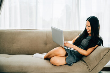 Wall Mural - Relaxed woman on sofa uses laptop for ecommerce watching videos learning. Engaged in studying success and relaxation at home. Modern technology for education and shopping.