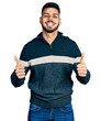 © Krakenimages.com - Young hispanic man with beard wearing casual winter sweater success sign doing positive gesture with hand, thumbs up smiling and happy. cheerful expression and winner gesture.