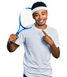 © Krakenimages.com - Young african american man playing tennis holding racket smiling happy pointing with hand and finger