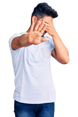 Poster - Handsome latin american young man wearing casual clothes covering eyes with hands and doing stop gesture with sad and fear expression. embarrassed and negative concept.