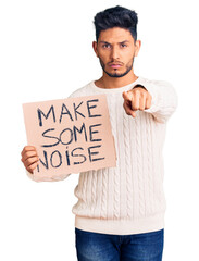 Wall Mural - Handsome latin american young man holding make some noise banner pointing with finger to the camera and to you, confident gesture looking serious