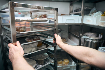 Cropped chef holding dishes on shelves in refrigerator storage in restaurant