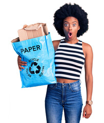 Sticker - Young african american woman holding recycling bag with paper and cardboard scared and amazed with open mouth for surprise, disbelief face