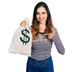 Wall Mural - Beautiful hispanic woman holding dollars bag pointing finger to one self smiling happy and proud