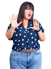 Poster - Young plus size woman wearing casual clothes afraid and terrified with fear expression stop gesture with hands, shouting in shock. panic concept.