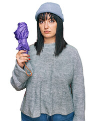 Canvas Print - Young hispanic woman holding closed purple umbrella thinking attitude and sober expression looking self confident