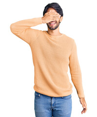 Canvas Print - Handsome hispanic man wearing casual sweater smiling and laughing with hand on face covering eyes for surprise. blind concept.