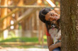 Frau mit braun-weissem Papillon-Hund sieht hinter einem Baum hervor und lächelt