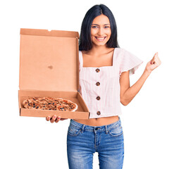 Sticker - Young beautiful latin girl holding delivery pizza box screaming proud, celebrating victory and success very excited with raised arms