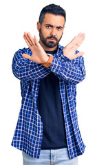 Sticker - Young hispanic man wearing casual clothes rejection expression crossing arms doing negative sign, angry face