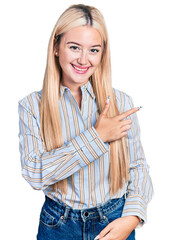 Poster - Beautiful blonde woman wearing casual striped shirt cheerful with a smile of face pointing with hand and finger up to the side with happy and natural expression on face