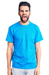 Wall Mural - Young handsome man with beard wearing casual t-shirt sticking tongue out happy with funny expression. emotion concept.