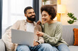 © Maria Vitkovska - Attractive smiling African American couple, handsome man and woman using laptop, working at home