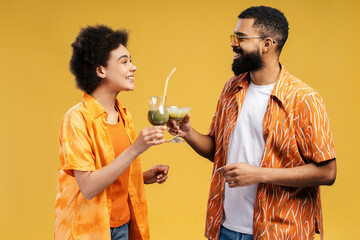 Smiling young African American man and woman wearing summer orange clothes holding cocktails talking