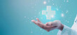 Hand holding medical cross symbol glowing on blue background