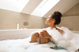 Fototapeta Boho - Woman relaxing in bathtub full of foam in bathroom of house