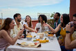 © CarlosBarquero - Laughing group of diverse young friends enjoying lunch together outdoors. Cheerful people gathered drinking red wine and eating snack on summer day having fun celebrating a birthday party on rooftop