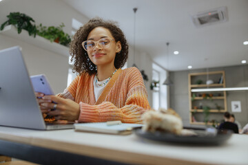 Wall Mural - a freelancer woman is sitting at a table using a laptop and a cell phone