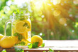 Dappled sunlight highlights a chilled mason jar of lemonade, complete with slices of lemon and fresh mint, set on a rustic wooden table.