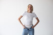 © kanashkin - Beautiful blonde girl in a white T-shirt and blue jeans and sneakers posing on a white background