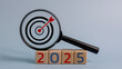 © FAMILY STOCK - A magnifying glass is on top of a pile of wooden blocks with the number 2025 on