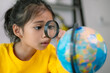 © FAMILY STOCK - A young girl is looking at a globe through a magnifying glass