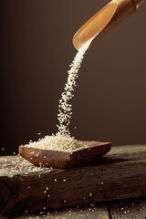 Poster - Grains of white sesame are poured with a wooden spoon in the wooden dish.