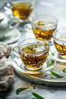 In this beautifully composed image, four cups of golden herbal tea are elegantly arranged on a marble tray, adorned with fresh green leaves. The soft lighting creates a warm and inviting ambiance