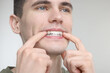 © New Africa - Young man applying whitening strip on his teeth against light grey background, closeup. Space for text