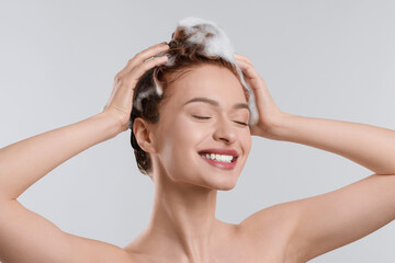 Canvas Print - Happy young woman washing her hair with shampoo on light grey background